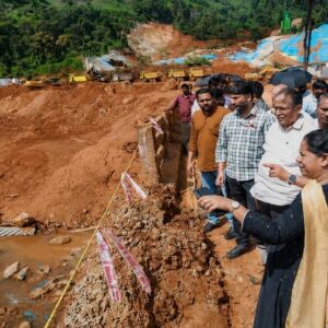 A large mound of excavated soil near a rehabilitation township construction site overlooking residential houses in Kalpetta, highlighting potential landslide risks to nearby families.